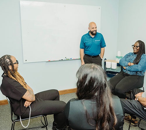 Pivotal Health staff seated in a small group session with a facilitator standing by a whiteboard