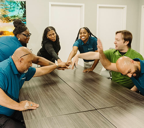 Pivotal Health team members joining hands in a group huddle around a conference table.
