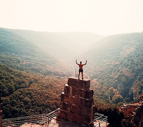Person standing triumphantly on a stone structure overlooking a vast, mountainous valley
